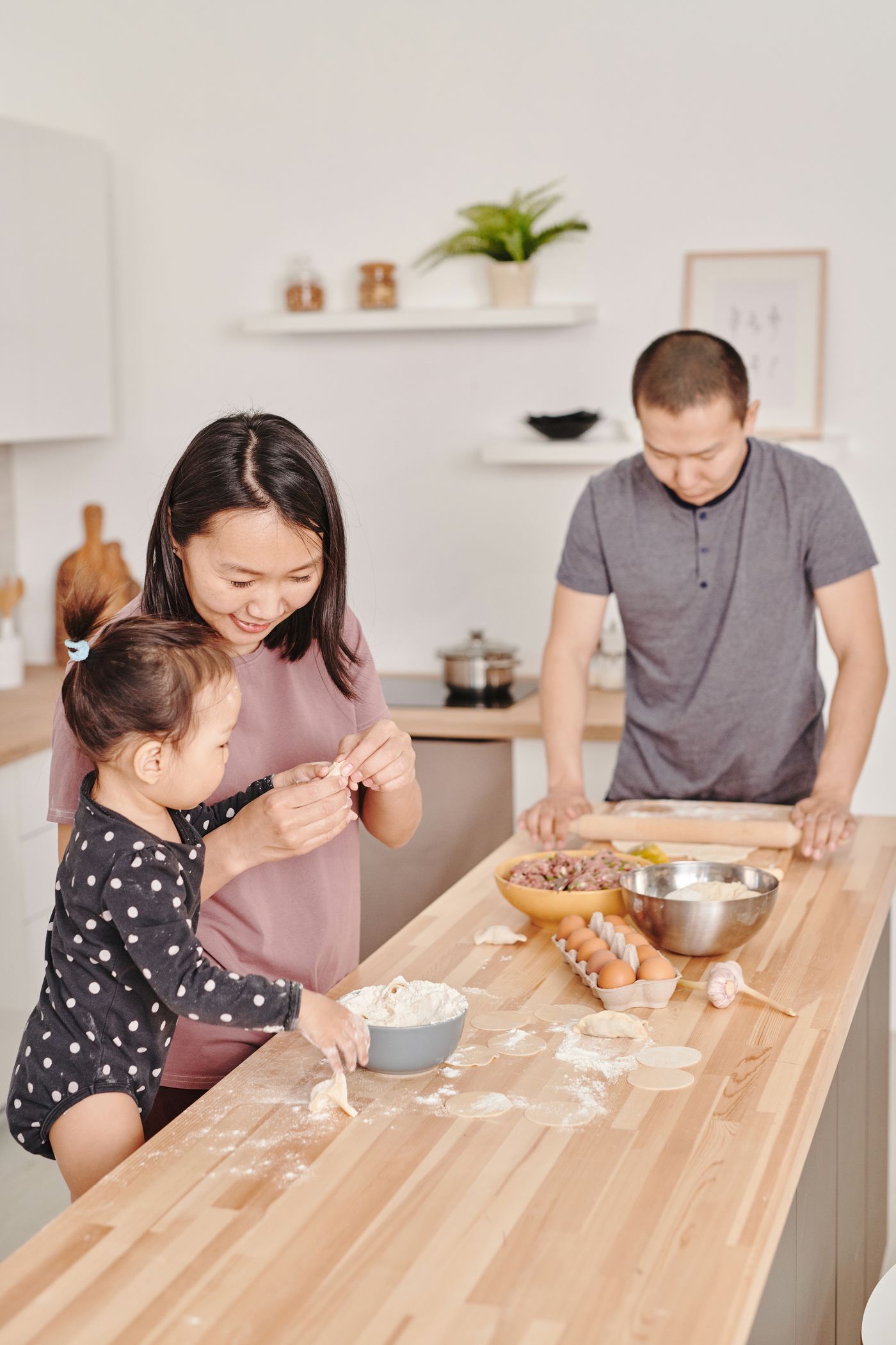 一家人在厨房一起准备饭菜，孩子和父母共同包饺子